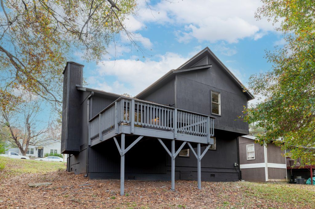 A black house with a large deck is sitting on top of a lush green field.